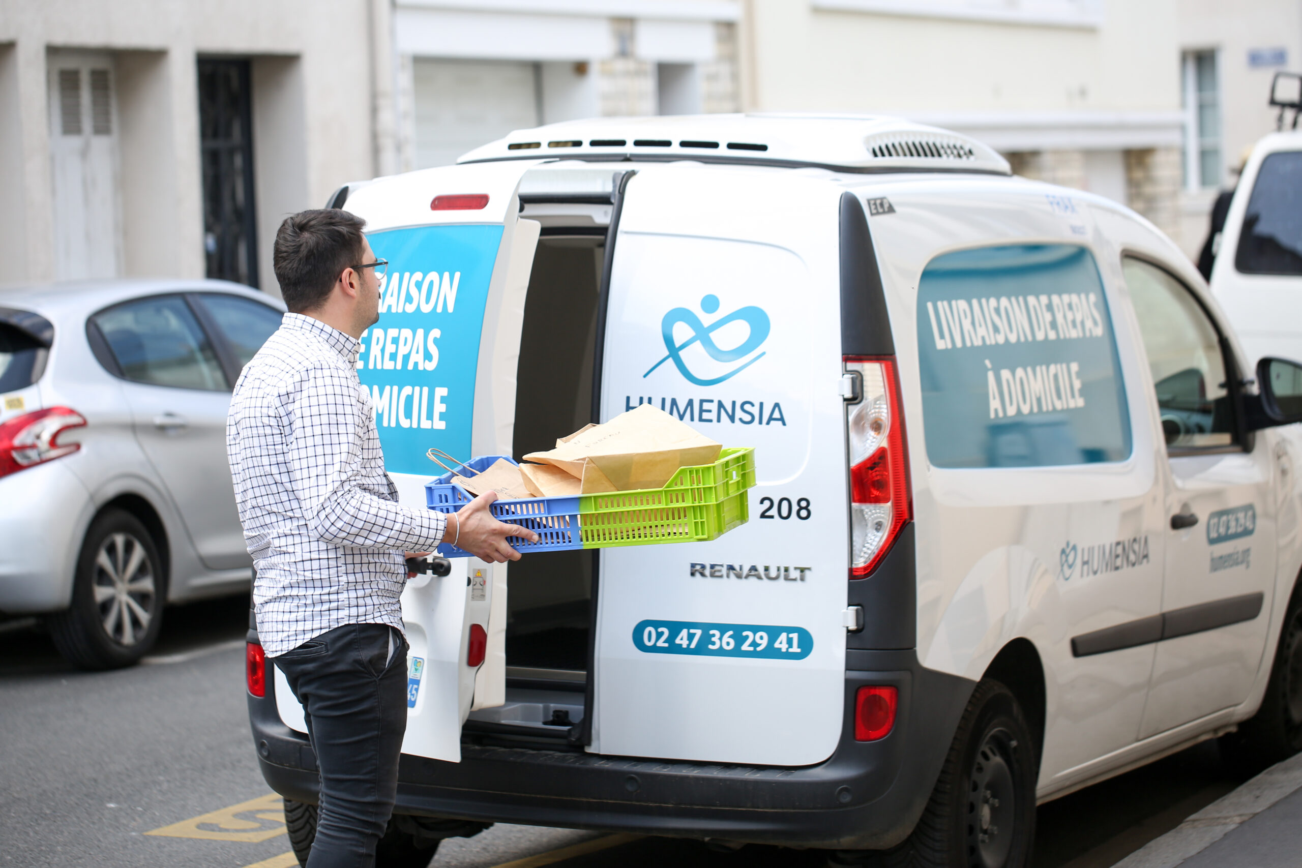 homme avec une cagette de repas devant le véhicule de livraison de repas à domicile